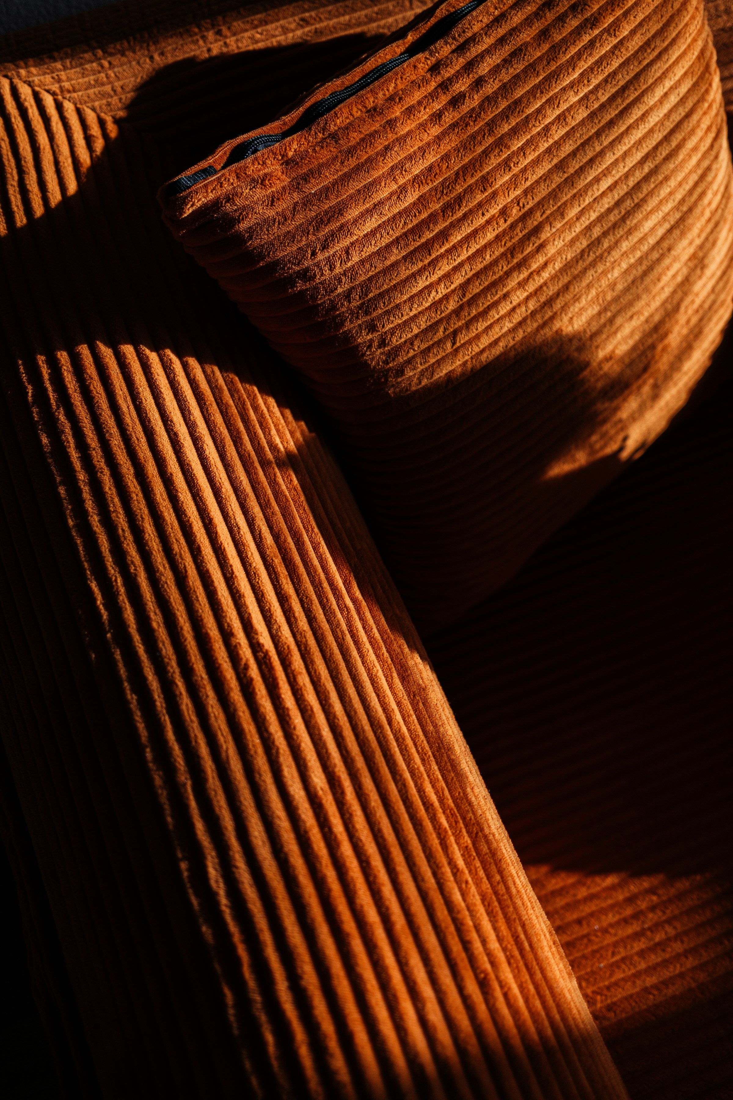 Primo piano di un cuscino e di un bracciolo in velluto a coste larghe color terracotta, in luce radente